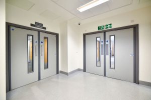 Two sets of grey fire doors positioned in what appears to be a hospital setting.