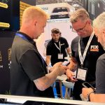 Three men engaged in a conversation at trade show booth.