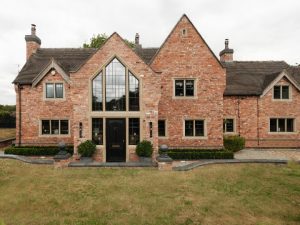 Red brick period home with a tall arched glass gable above a black front door, framed in stone-effect surrounds