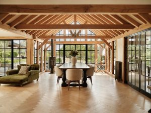 Light-filled oak-framed room with exposed vaulted beams, black steel-framed glazing and a dining table on herringbone flooring