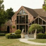 Red brick house with a gabled glass extension and steel framed windows, set behind clipped hedges.