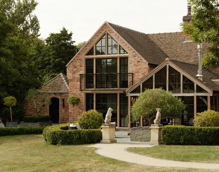 Red brick house with a gabled glass extension and steel framed windows, set behind clipped hedges.