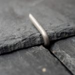 Close-up of a Roof Tingle securing a slate, bent over the slate edge to hold it firmly in place without nails or upward pressure.