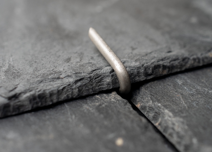 Close-up of a Roof Tingle securing a slate, bent over the slate edge to hold it firmly in place without nails or upward pressure.
