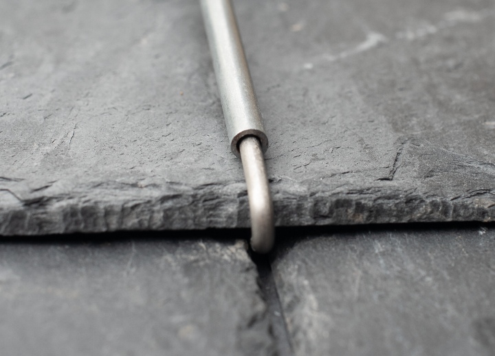 Close-up showing a Roof Tingle passing over the edge of a slate, preventing movement while leaving the slate in its natural position.